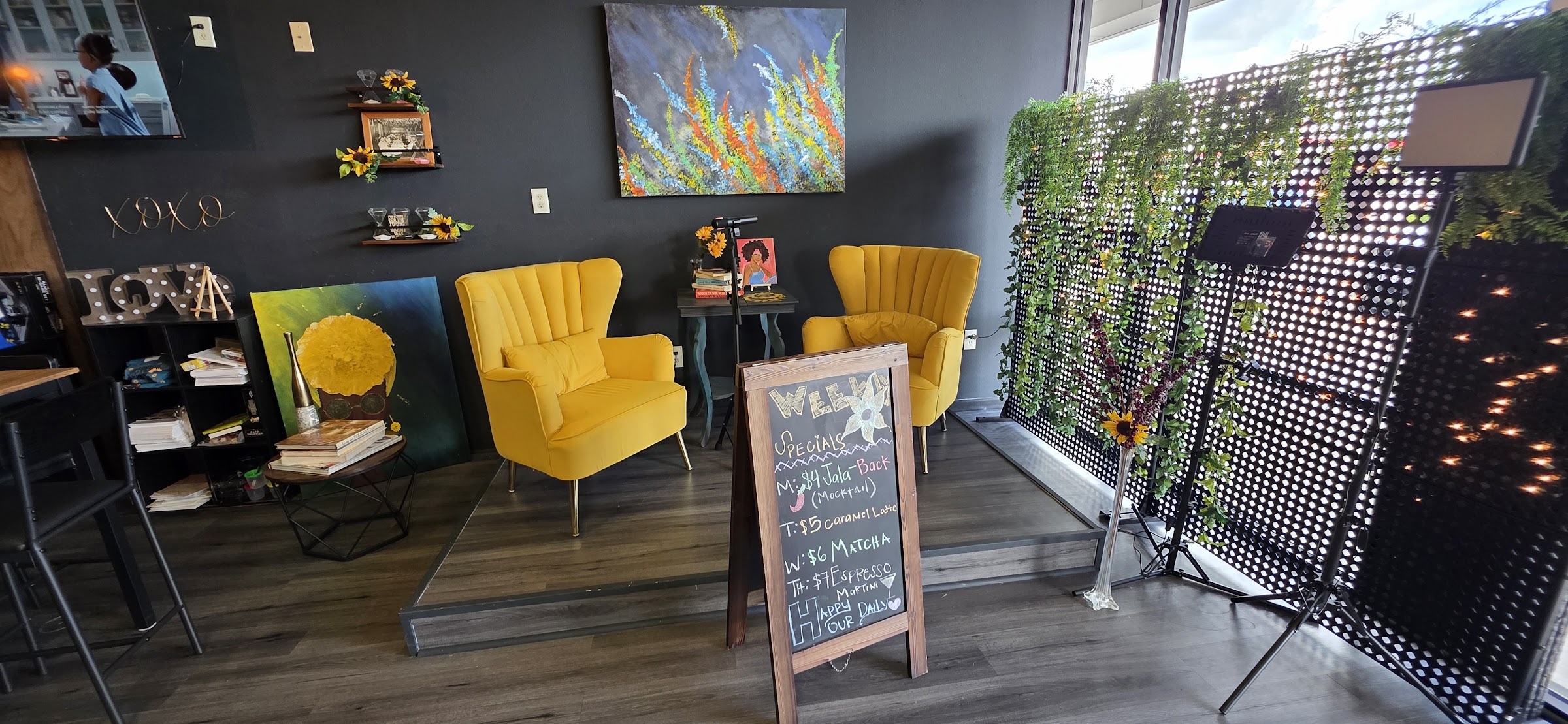 Small performance stage with yellow wingback chairs, microphone, colorful art, and chalkboard sign.