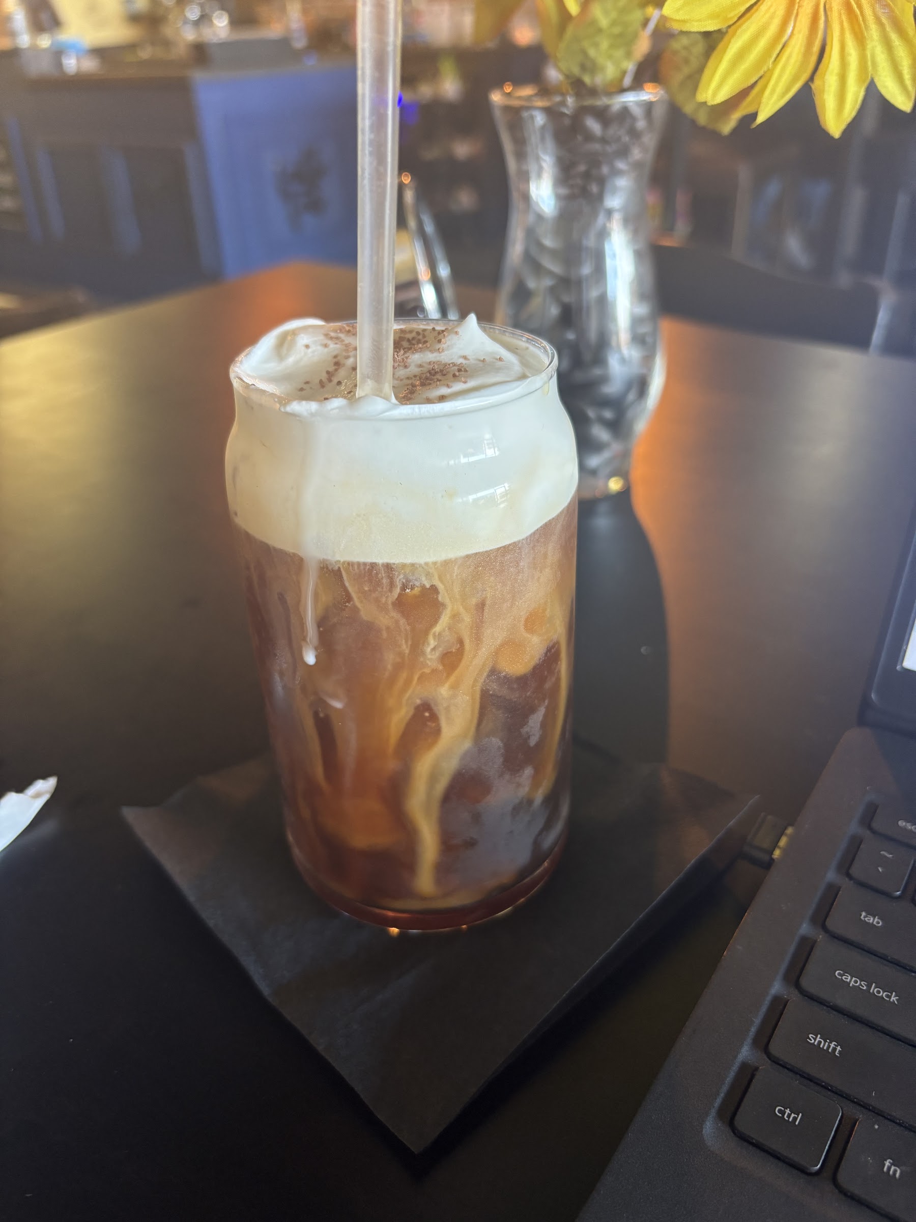 Iced coffee topped with cold foam beside an open laptop