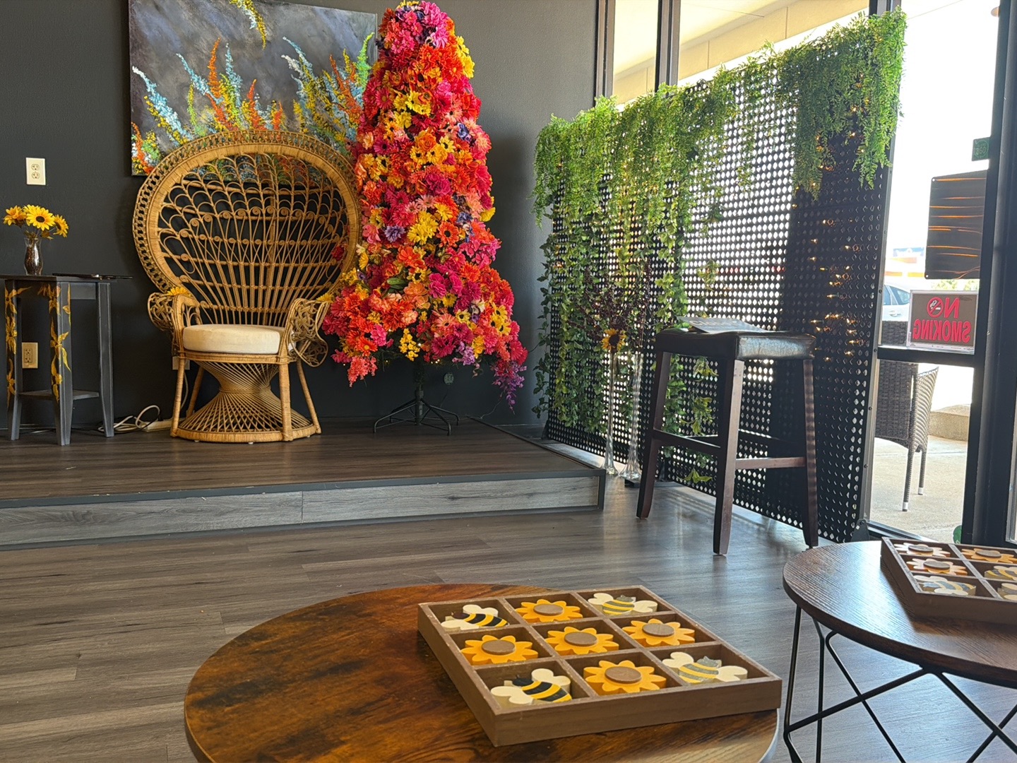 Stage area with wicker peacock chair, floral arrangement, and games on tables.